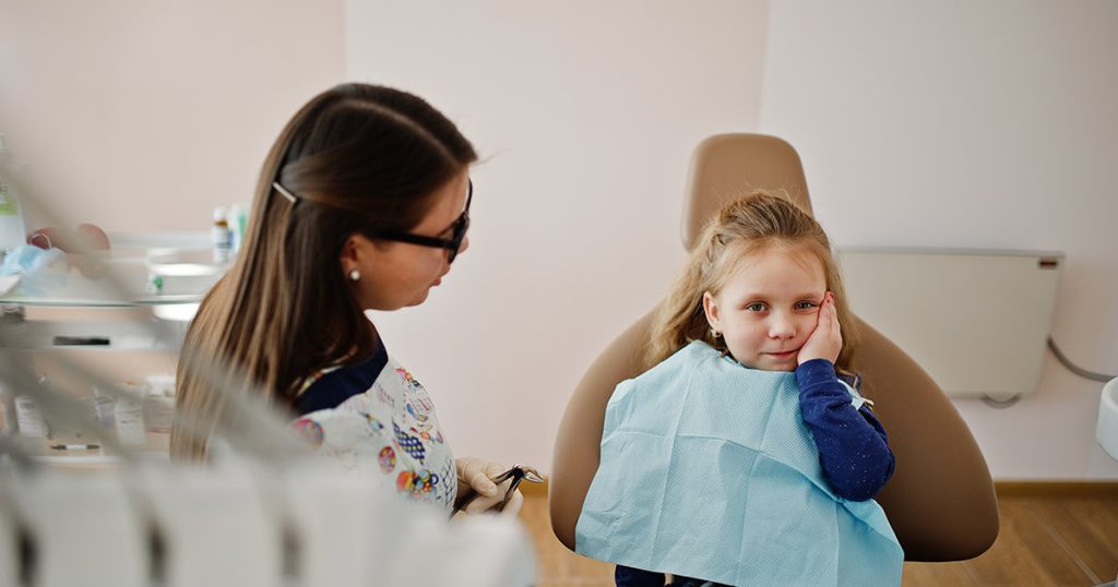 Odontopediatra atendiendo a niña con caries producida en los dientes de leche.
